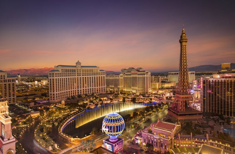 Stunning aerial view of Las Vegas skyline at sunset, featuring the Eiffel Tower and Bellagio fountains.